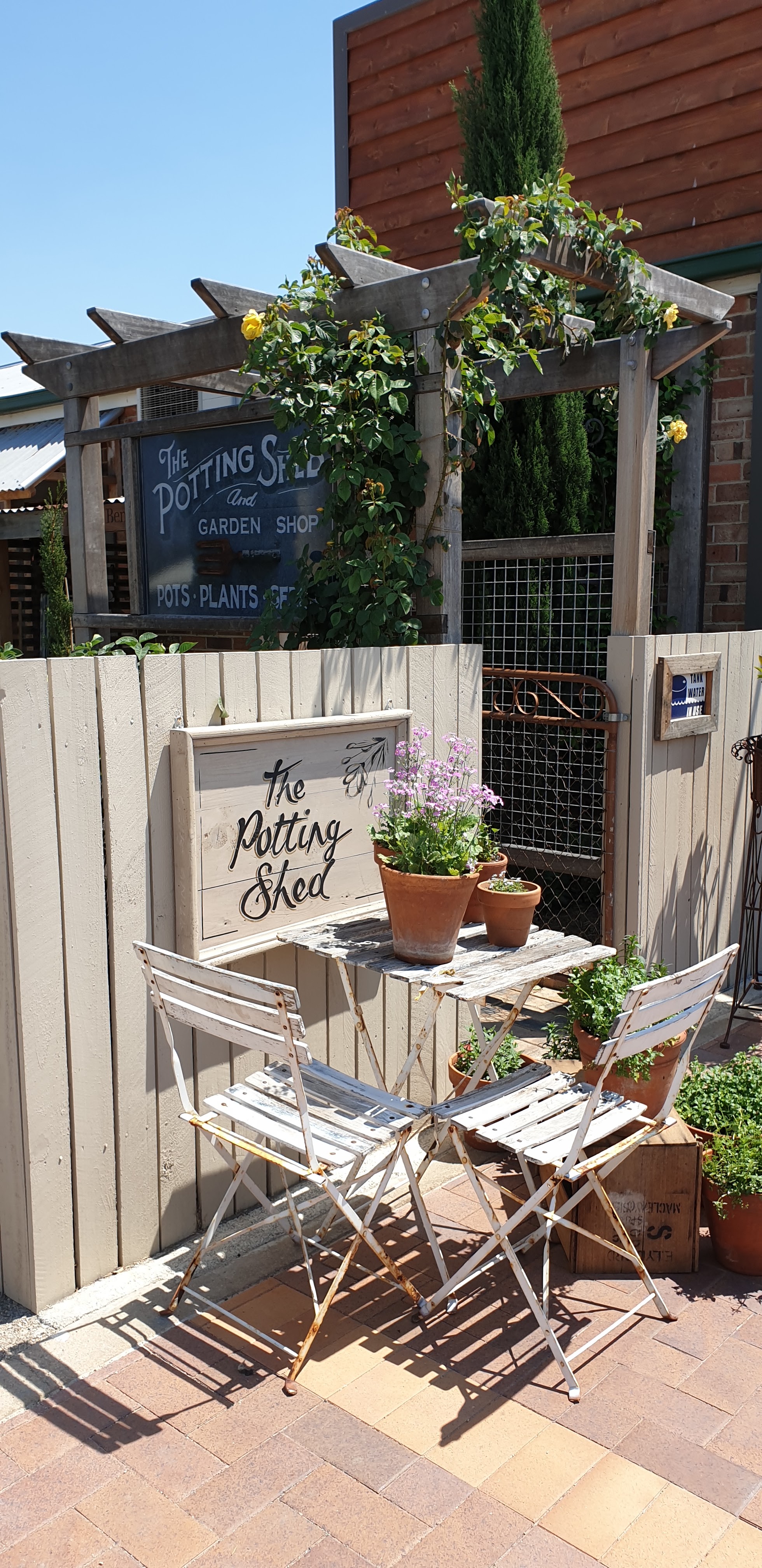 White bistro table and chairs beside the hand-lettered Potting Shed sign