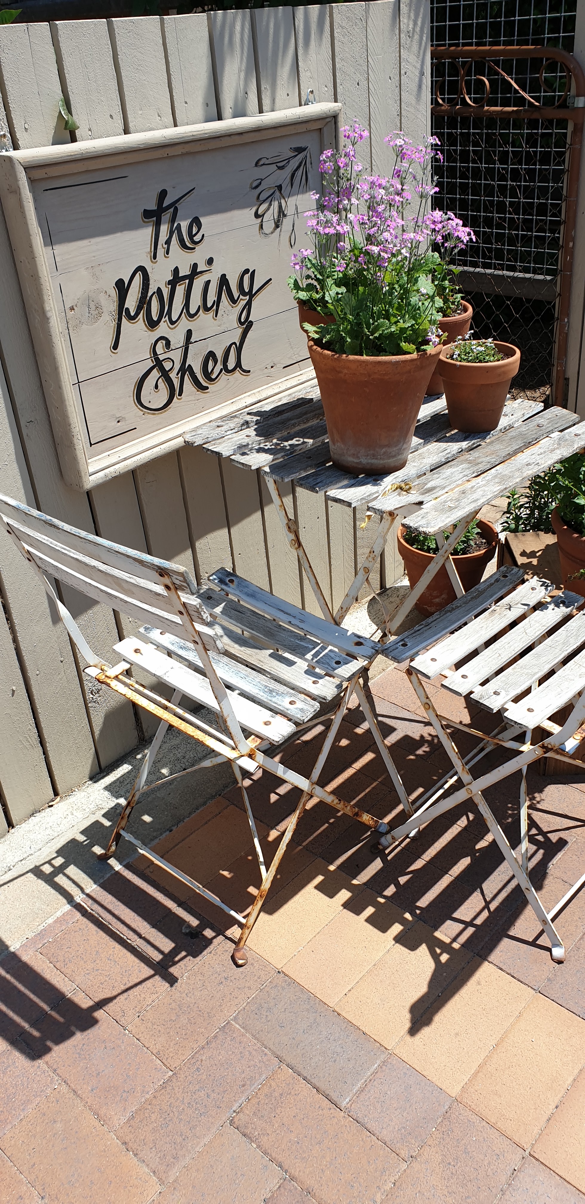 The Potting Shed sign with terracotta pots of purple flowers